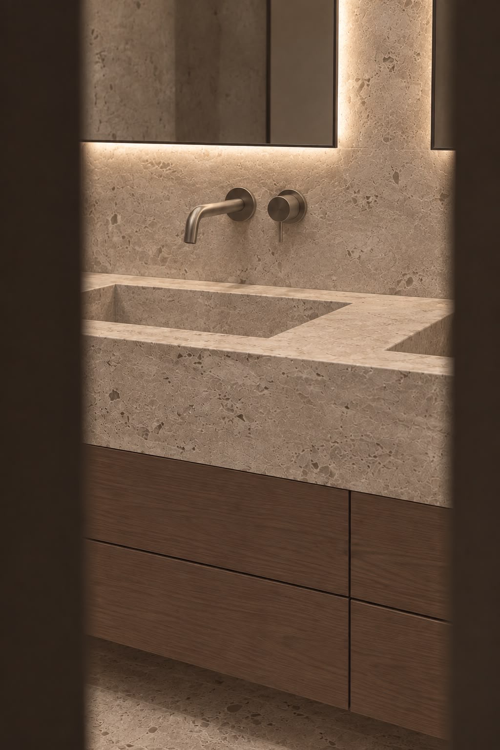 A travertine basin, a bronze-toned wall tap and walnut drawers, seen through the door. Render.