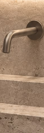 A detail: a bronze-toned wall tap on travertine. Render.